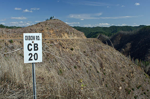OR: South Coast Region, Douglas County, Coast Range, Smith River Area, Smith River Side Roads, Oxbow Road, Oxbow Road crosses the Pacific Divide in a clearcut. Forestry road sign indicates its name and that CB channel 20 is monitored for logging trucks. [Ask for #276.066.]
